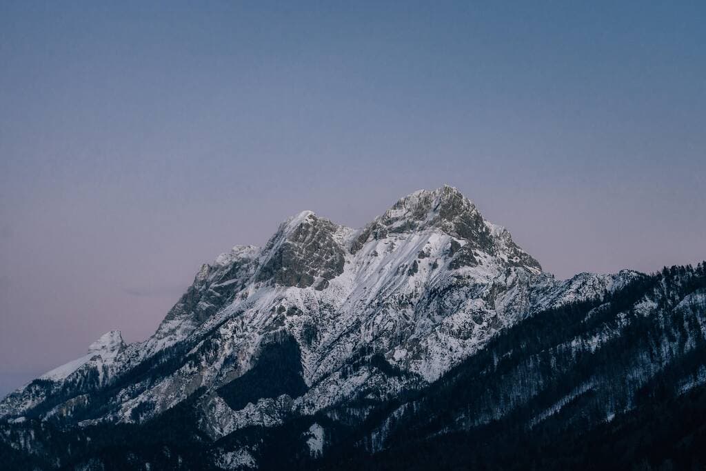 Snow-covered mountain range at dusk with a clear sky in the background